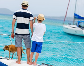 Mann mit Kind und Hund an Deck eines Segelboots